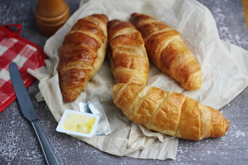 A pile of delicious fresh croissants served with butter on a gray table.