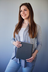 Obraz premium Smiling student or woman teacher wearing cassual holding book looking away. Isolated portrait on gray.