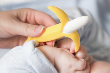 male baby holds banana teether in his hand, development and massage of the gums. close up teether