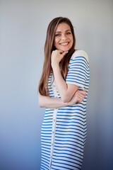Smiling woman in white long dress and brown hair standing with crossed arms. Woman teacher wearing white dress with blue stripes.