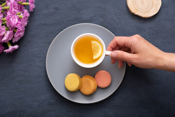 Smile with macaroons and female hand on a plate on a dark stone table with flowers