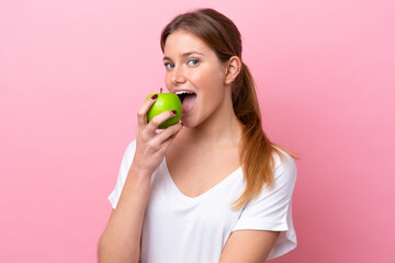 Young caucasian woman isolated on pink background eating an apple