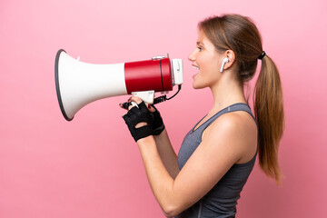 Young sport caucasian woman isolated on pink background shouting through a megaphone