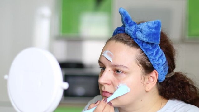 Woman using spatula to apply moisture anti-wrinkle mask before facial foundation, moisturizer cream, looking in mirror. Face skincare, professional mask product cosmetics. Non-surgical rejuvenation