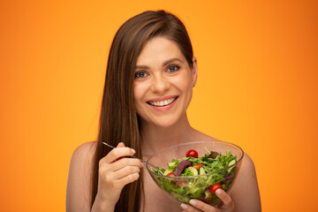 Smiling woman with naked shoulders holding bowl with green salad isolated on orange yellow background.