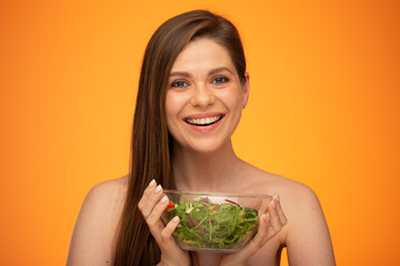 Happy woman with bare shoulders and long hair holding bowl with green salad and tomatoes isolated on orange yellow background.