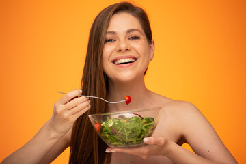 Woman with bare shoulders eating green salad isolated portrait on orange yellow background.