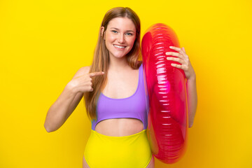 Young caucasian woman holding air mattress isolated on yellow background with surprise facial expression