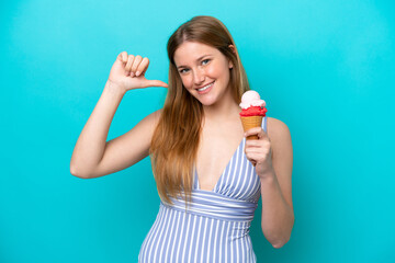 Young caucasian woman in swimsuit eating ice cream isolated on blue background proud and...