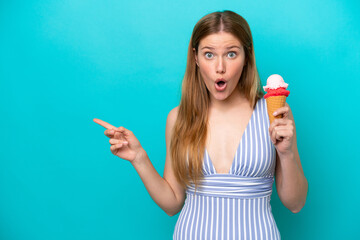 Young caucasian woman in swimsuit eating ice cream isolated on blue background surprised and...