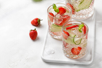 Delicious refreshing summer lemonade with strawberry, cucumber and basil in a glass with grops....