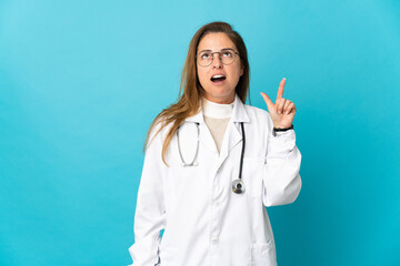 Middle age Brazilian doctor woman isolated on blue background thinking an idea pointing the finger up