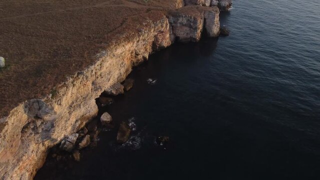 Drone top down aerial view of waves splash against rocky seashore, background. Flight over high cliffs of sea coast. Camera move forward.