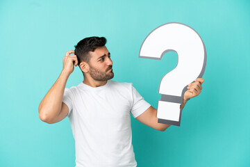 Young handsome caucasian man isolated on blue background holding a question mark icon and having...