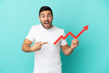 Young handsome caucasian man isolated on blue background holding a catching a rising arrow with surprised expression