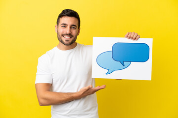 Young handsome caucasian man isolated on yellow background holding a placard with speech bubble icon with happy expression