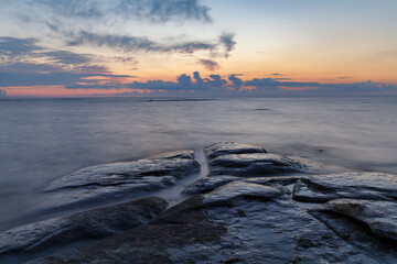 Boulders and rocks in the surf on coast of the Baltic sea at sunset, long exposure