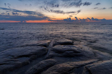 Obraz premium Boulders and rocks in the surf on coast of the Baltic sea at sunset, long exposure