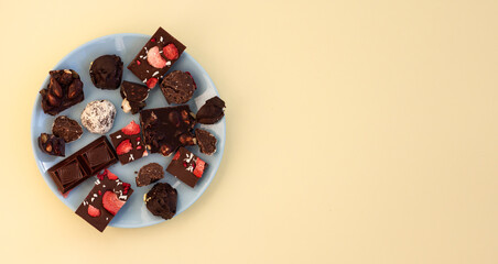 top view of pieces of different chocolates on blue plate, handmade craft chocolate and praline broken into pieces, copy space, template or confectionery banner