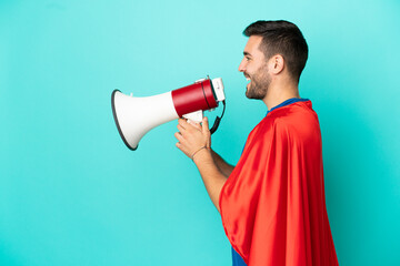 Super Hero caucasian man isolated on blue background shouting through a megaphone