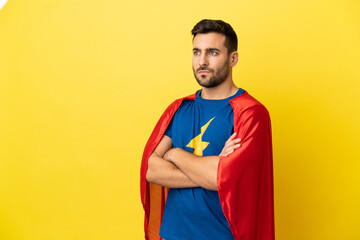 Young handsome caucasian man isolated on yellow background in superhero costume with arms crossed