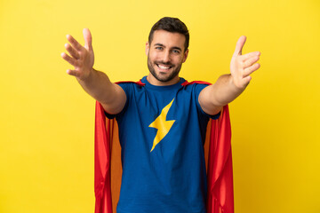 Young handsome caucasian man isolated on yellow background in superhero costume and doing coming gesture