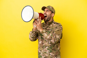 Military man isolated on yellow background shouting through a megaphone