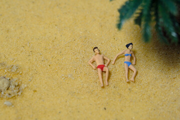 Fototapeta na wymiar Miniature people toy figure photography. Top eagle view of men and girl couple relaxing, lying at beach sand when daylight at seaside
