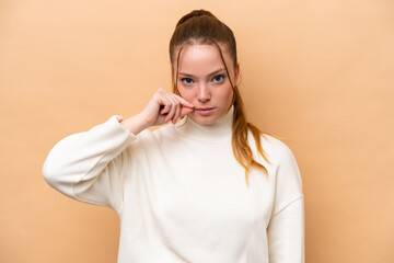 Young caucasian woman isolated on beige background showing a sign of silence gesture