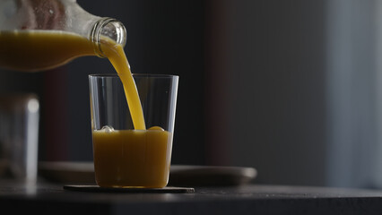 Man pour orange mango juice in tumbler glass on kitchen countertop