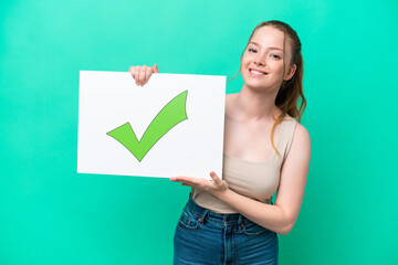 Young caucasian woman isolated on green background holding a placard with text Green check mark icon with happy expression