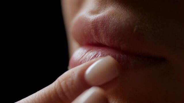 Macro shot of white-skinned female model strokes her lower lip on black background | Lip texture shot for lip care products commercial