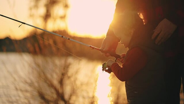 father is teaching his little son to catch fish by fishing rod, dad and child are spending time together