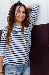 a girl with a dreadlocked hairstyle poses in the summer outdoors, dressed in a T-shirt and denim shorts