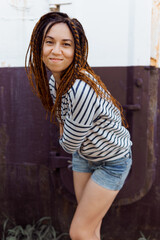 Naklejka premium a girl with a dreadlocked hairstyle poses in the summer outdoors, dressed in a T-shirt and denim shorts
