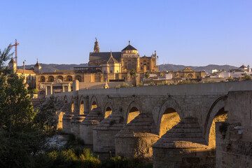 The first sunrays shine through the arches of the ancient roman stone bridge over the Guadalquivir river in the morning hours, Cordoba, Spain