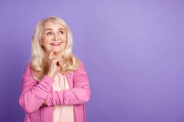 Photo of senior cheerful woman hand touch chin look empty space dream think idea isolated over purple color background