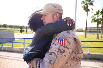 Afro-American woman and American soldier who has just arrived from the war on a peace mission embrace each other tightly. The woman is happy. Concept war and army, peace and mission.