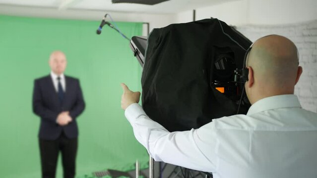 A cameraman counting in for live News TV in green screen video studio. A male presenter is talking using a teleprompter