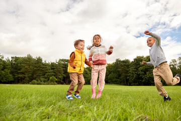 childhood, leisure and people concept - group of happy children playing and jumping at park