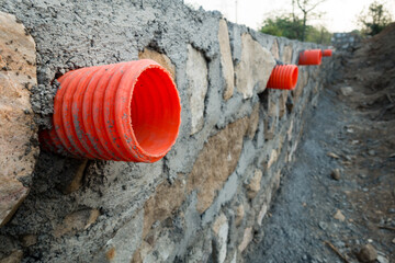 A row of orange culverts or water outlet pipes through a stone retaining wall for storm drainage in...