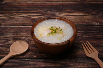 Nutritious rice porridge with soft boiled egg and spring onion in wooden bowl for breakfast or light meal