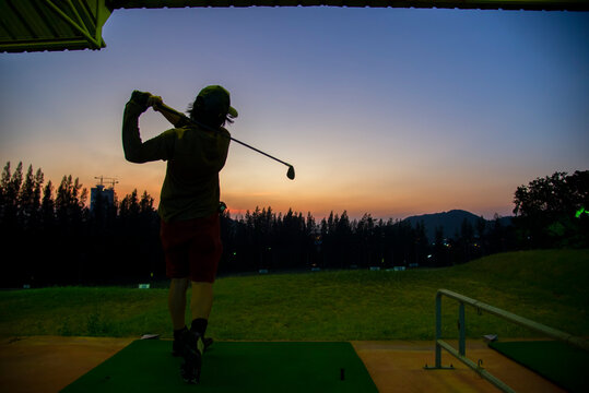 Asian golfer Man swing golf ball practice at golf driving range on evening on time for healthy sport. Lifestyle and Sport Concept