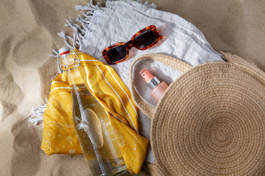 leisure and summer holidays concept - sunscreen in bag, sunglasses, bottle of water, pareo and beach blanket on sand