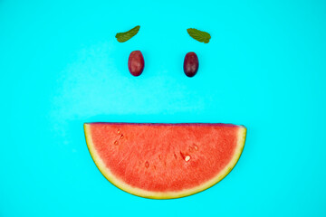 Slice of watermelon accompanied by 2 red grapes and 2 mint leaves, simulating a smiling face.