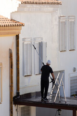 Man washing facade of house with pressure washer