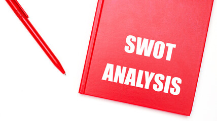 The text SWOT ANALYSIS is written on a red notepad near a red pen on a white table in the office. Business concept