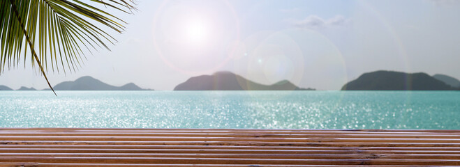 empty bamboo wooden table with palm branches on beautiful blur defocused blue sea background.