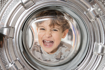 View from inside the washing machine. A boy with curly hair puts head inside the drum makes a...