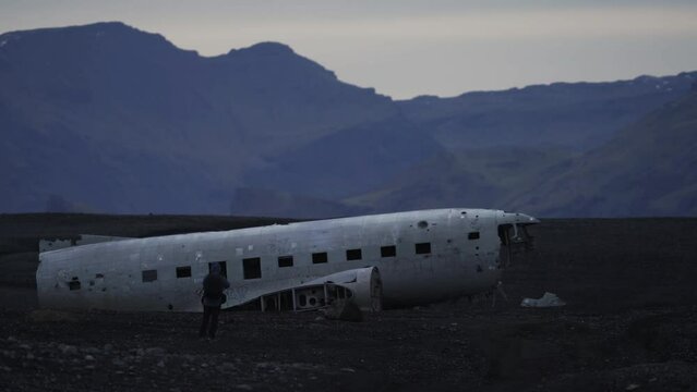 Rear view of unrecognizable tourist taking photos of airplane wreck